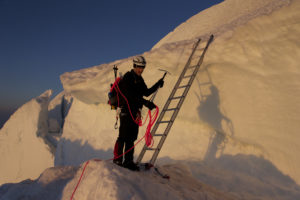 Man uses ice picks, rope, and a ladder to ascend a tricky mountain of snow